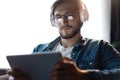 Handsome young man in casual clothes using a digital tablet and headphones and smiling while sitting on the chair. Royalty Free Stock Photo