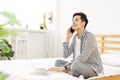 Handsome young man in casual clothes and working at home while sitting on the bed,with a laptop and talking on phone in bedroom