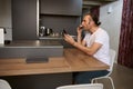 Handsome young man checking his messages, reading social media news over a cup of freshly brewed espresso coffee at home