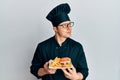 Handsome young man chef holding burger with fries smiling looking to the side and staring away thinking Royalty Free Stock Photo