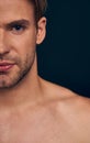 Handsome young man . Cropped image of shirtless muscular man is standing on dark blue background. Half face Royalty Free Stock Photo