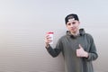A handsome young man with a cup of coffee in his hands shows a thumbs up on a light background Royalty Free Stock Photo