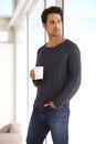 Handsome, young and man with a cup of coffee standing by the window in a vacation house. Calm, relax and attractive male