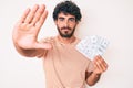 Handsome young man with curly hair and bear holding money bag with dollar symbol with open hand doing stop sign with serious and Royalty Free Stock Photo