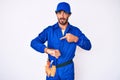 Handsome young man with curly hair and bear weaing handyman uniform in hurry pointing to watch time, impatience, upset and angry Royalty Free Stock Photo
