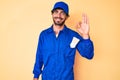 Handsome young man with curly hair and bear wearing builder jumpsuit uniform smiling positive doing ok sign with hand and fingers Royalty Free Stock Photo