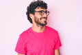 Handsome young man with curly hair and bear wearing casual clothes and glasses looking away to side with smile on face, natural Royalty Free Stock Photo