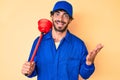 Handsome young man with curly hair and bear wearing plumber uniform holding toilet plunger celebrating achievement with happy Royalty Free Stock Photo