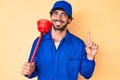 Handsome young man with curly hair and bear wearing plumber uniform holding toilet plunger smiling with an idea or question Royalty Free Stock Photo