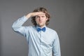 Handsome young man with dark curly hair wearing blue shirt and bow tie putting hand on his forehead and smiling, looking far