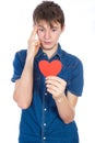 Handsome young man in denim blue shirt standing on a white background with a red paper heart in hands.