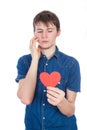 Handsome young man in denim blue shirt standing on a white background with a red paper heart in hands.