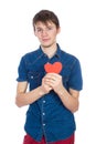 Handsome young man in denim blue shirt standing on a white background with a red paper heart in hands.