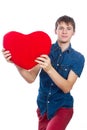 Handsome young man in denim blue shirt standing on a white background with a red paper heart in hands.