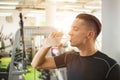 Handsome young man drinking water from a bottle and taking a break from exercising in a gym. Royalty Free Stock Photo