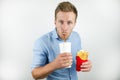 Handsome young man drinks soda from papper cup and holds fries from fast food restaurant on isolated white background Royalty Free Stock Photo