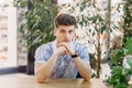 A handsome young man with an earring in his ear sits at the table with his hands folded and looks at the camera