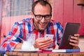 Handsome young man eating sandwich in restaurant. He is holding a phone and tablet.