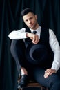 Handsome young man in elegant suit with hat in hands on black background