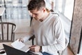 Handsome young man entrepreneur with a laptop in a stylish shirt is writing in a notebook sitting in a cafe Royalty Free Stock Photo