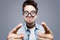 Handsome young man with funny glasses joking and making funny face over gray background. Royalty Free Stock Photo