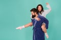 Handsome young man giving his girlfriend piggyback ride. Couple in bathrobes having fun turquoise background. Lets stay Royalty Free Stock Photo