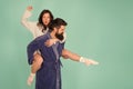 Handsome young man giving his girlfriend piggyback ride. Couple in bathrobes having fun turquoise background. Lets stay Royalty Free Stock Photo