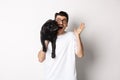 Handsome young man in glasses holding his black pug and waving hand, guy saying hello while carry dog with one arm Royalty Free Stock Photo