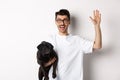 Handsome young man in glasses holding his black pug and waving hand, guy saying hello while carry dog with one arm Royalty Free Stock Photo