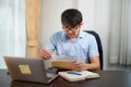 A handsome young man in glasses showing amazing expression while reading acceptance letter with laptop on desk at home Royalty Free Stock Photo