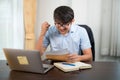 A handsome young man in glasses showing surprised expression while reading acceptance letter with laptop on desk at home Royalty Free Stock Photo