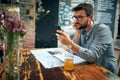 Handsome young man with glasses sitting in cafe using smarphone and listening with earphones