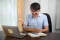 A handsome young man in glasses succeeds while reading acceptance letter with a laptop on his desk at home Royalty Free Stock Photo