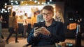 Handsome Young Man in Glasses is Using a Smartphone while Sitting at a Table in a Outdoors Street Royalty Free Stock Photo