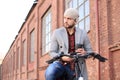 Handsome young man in grey coat and hat looking at phone while sitting on his bicycle Royalty Free Stock Photo