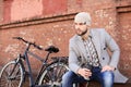 Handsome young man in grey coat and hat sitting on a bench relaxed drinking coffee and thinking near his bicycle Royalty Free Stock Photo