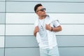 Handsome young man hipster with a white sweatshirt in a vintage T-shirt in stylish sunglasses with a fashionable hairstyle posing Royalty Free Stock Photo