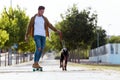 Handsome young man with his dog skateboarding in the park. Royalty Free Stock Photo