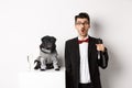 Handsome young man and his puppy celebrating New Year holiday, black pug and dog owner standing in suits, guy holding Royalty Free Stock Photo