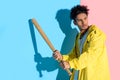 Handsome young man holding baseball bat in hands about to kick and looking away on pink and blue Royalty Free Stock Photo