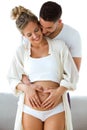Handsome young man holding belly of his pregnant wife making heart together at home