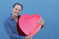 Handsome young man holding big red heart symbol on blue background Royalty Free Stock Photo