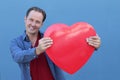 Handsome young man holding big red heart symbol on blue background Royalty Free Stock Photo