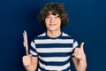 Handsome young man holding paintbrushes smiling happy and positive, thumb up doing excellent and approval sign Royalty Free Stock Photo