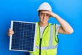 Handsome young man holding photovoltaic solar panel stressed and frustrated with hand on head, surprised and angry face Royalty Free Stock Photo