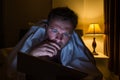 Handsome young man at home reading with tablet PC lying on bed at night. He is tired and want to sleep Royalty Free Stock Photo