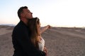 Handsome young man hugging his girlfriend in white dress, she pointing and looking into the distance, couple standing Royalty Free Stock Photo