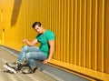 Handsome young man with inline roller skates sitting near yellow building Royalty Free Stock Photo