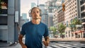 Handsome Young Man is Jogging on a Street of a Big City Center. Male is Running in Blue T-Shirt, Royalty Free Stock Photo