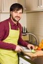 Handsome young man in the kitchen with apron cutting vegetables Royalty Free Stock Photo